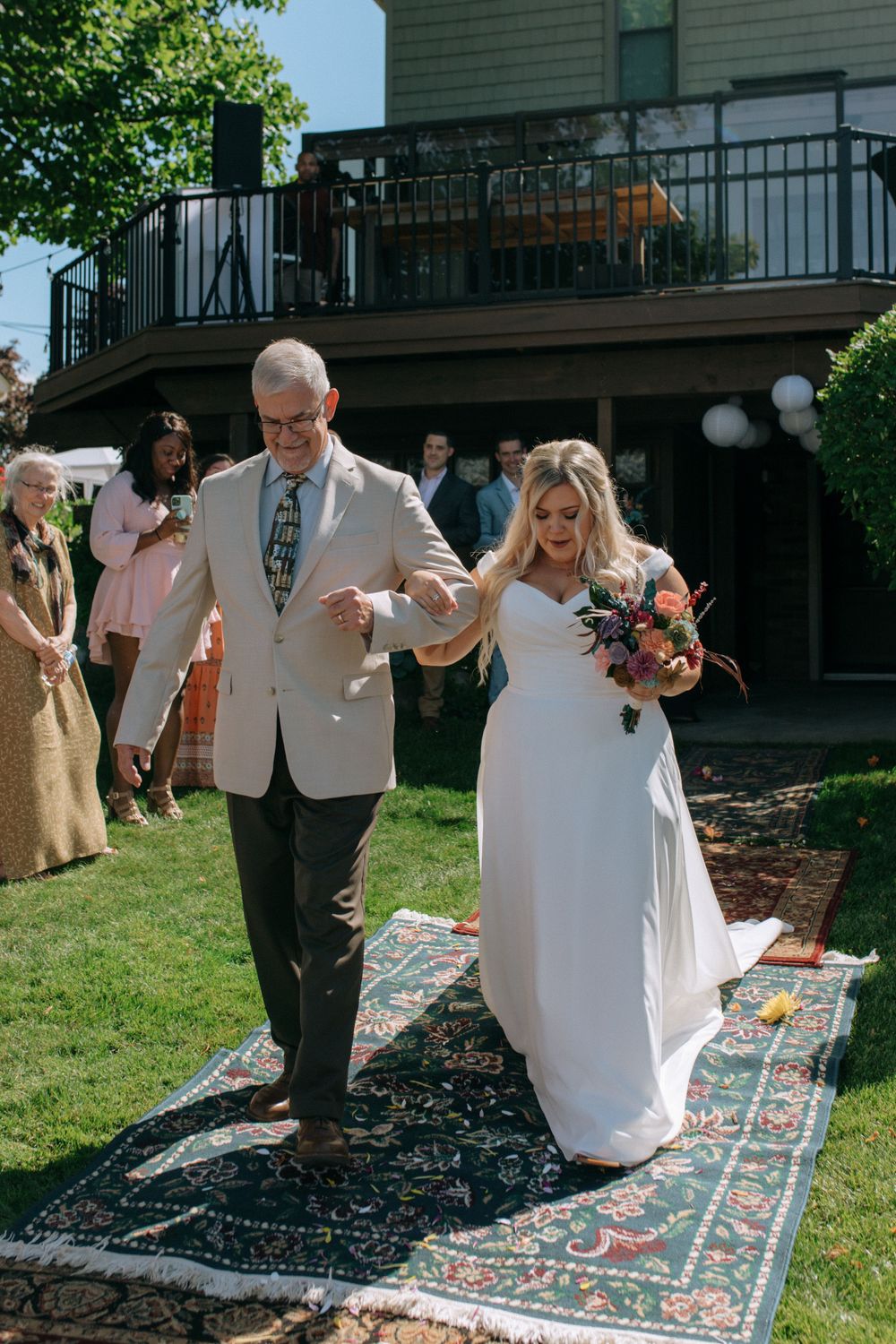 A wedding ceremony procession walking down a decorative rug path outdoors.