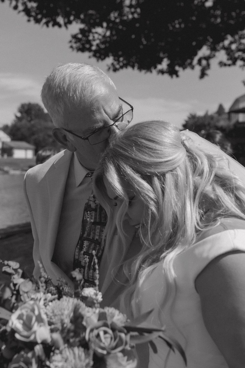 Black and white photo of an emotional moment between the bride and an elderly man holding flowers.
