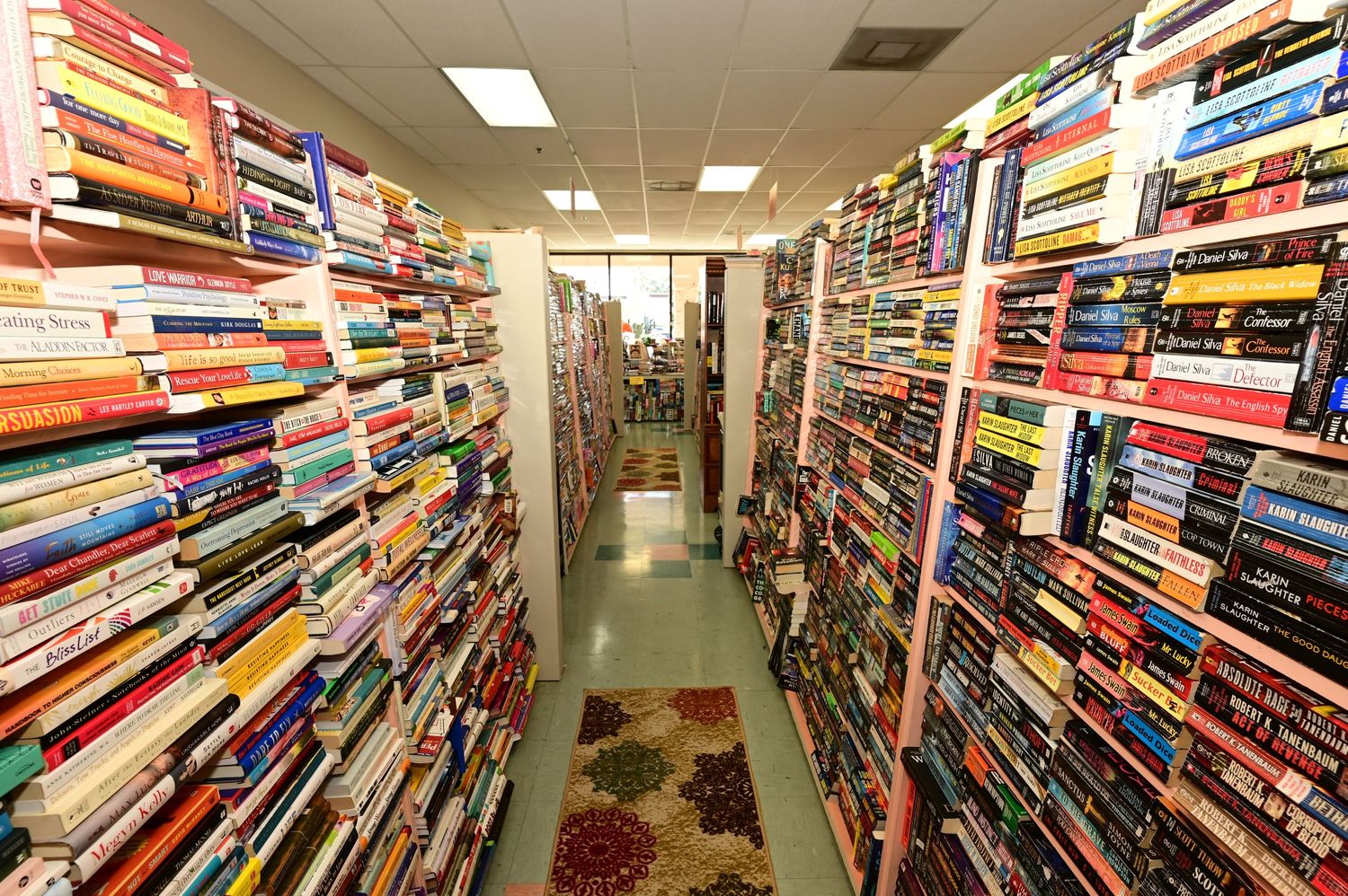 Long perspective shot down a bookstore aisle showing densely packed shelves and carpeted flooring.