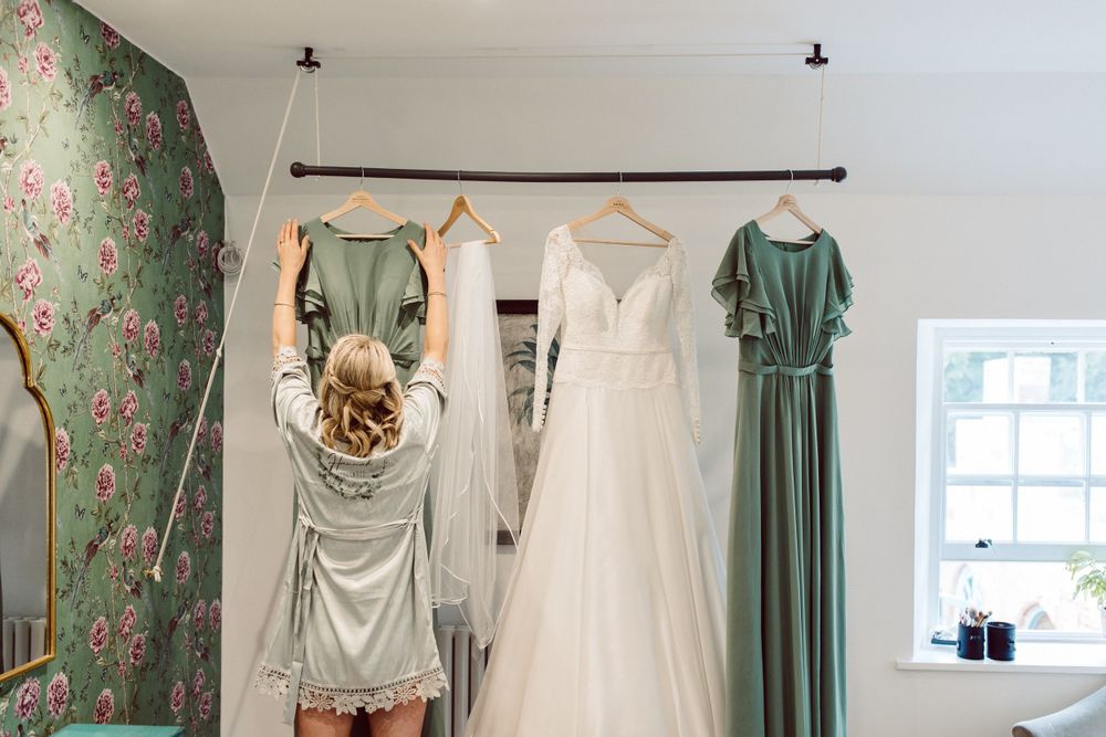 Wedding dresses and bridesmaid gowns displayed in a bright room with floral wallpaper.