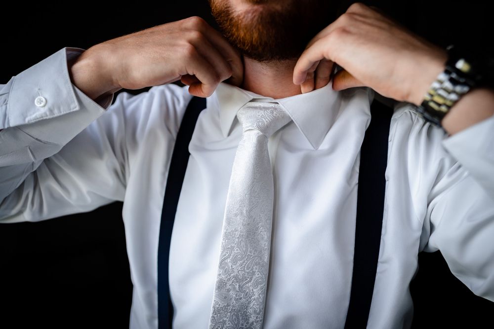Close-up shot of formal attire details including a silver tie and white dress shirt being adjusted.