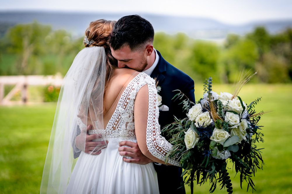 Romantic wedding couple embracing outdoors with elegant white dress and floral details.