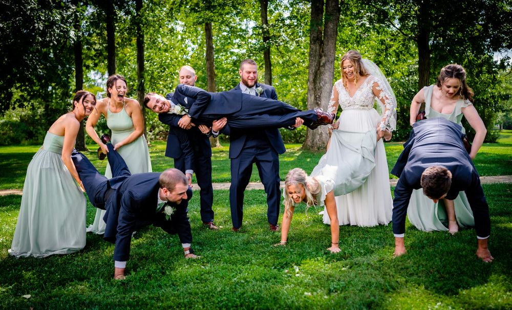 Wedding party lounging on grass in formal attire during outdoor photo session.