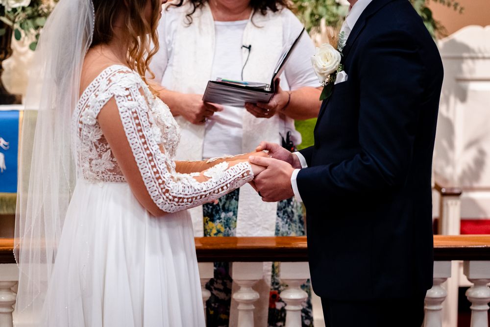 Close-up of wedding ceremony ring exchange with white lace dress details.