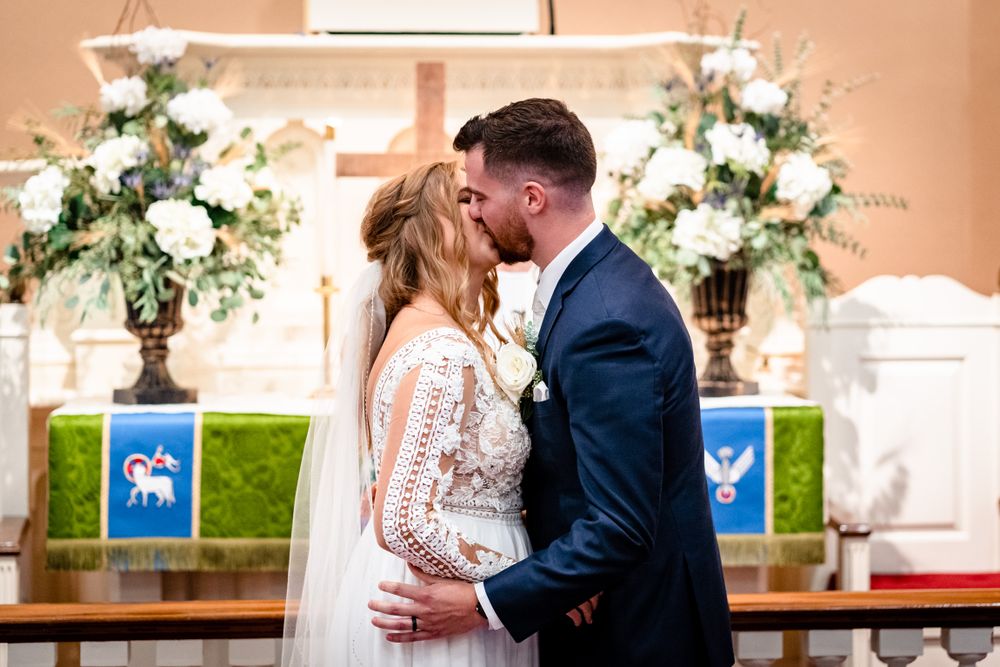 Wedding ceremony moments captured in church with white floral arrangements and blue banners.