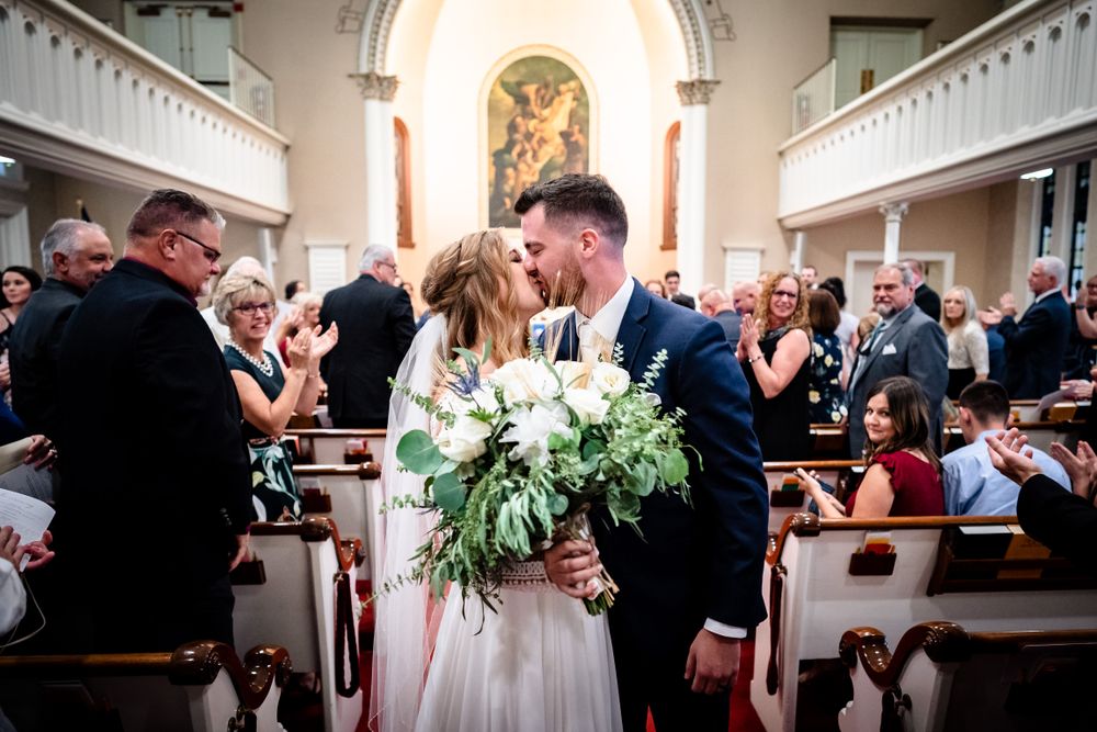 Wide angle view of church wedding ceremony with guests seated in wooden pews.