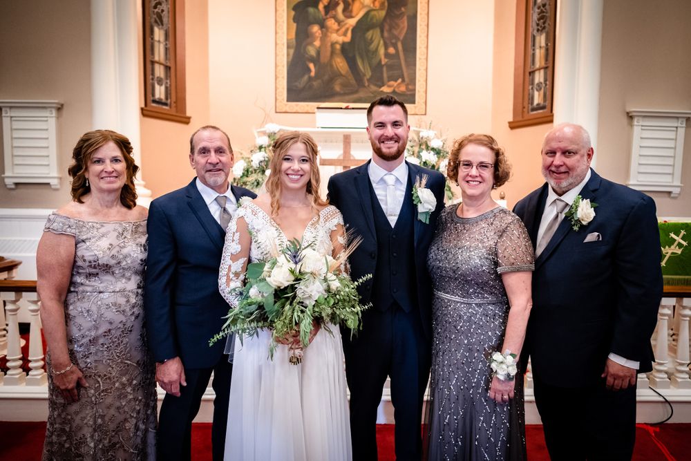 Wedding party members in navy suits and sparkly dresses pose together in an elegant indoor venue.