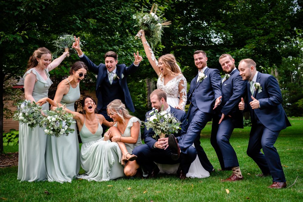 Wedding party lounges casually on grass for fun group photos outdoors.