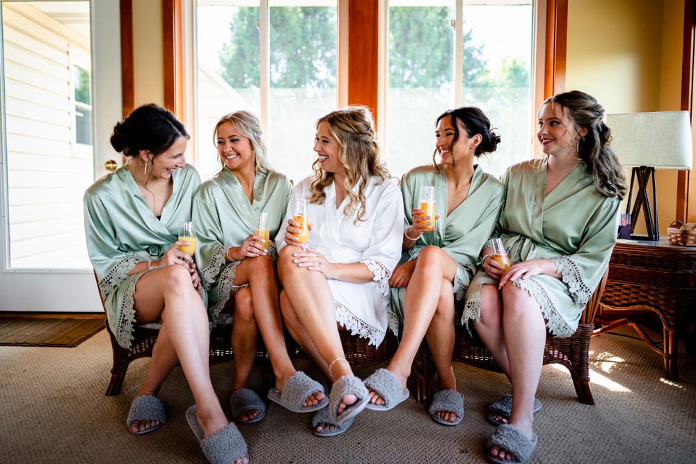 Candid group sitting together by window in matching robes during wedding preparations.