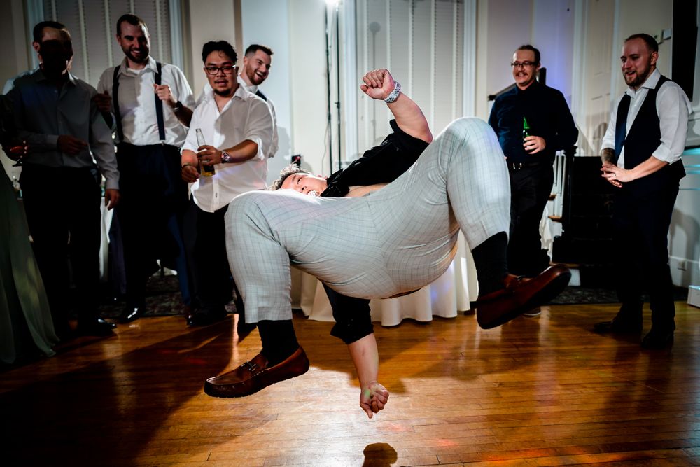Wedding party performing energetic dance moves on a wooden dance floor.