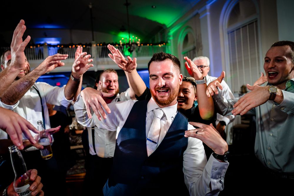 Panoramic shot of wedding guests celebrating on the dance floor with dramatic lighting.