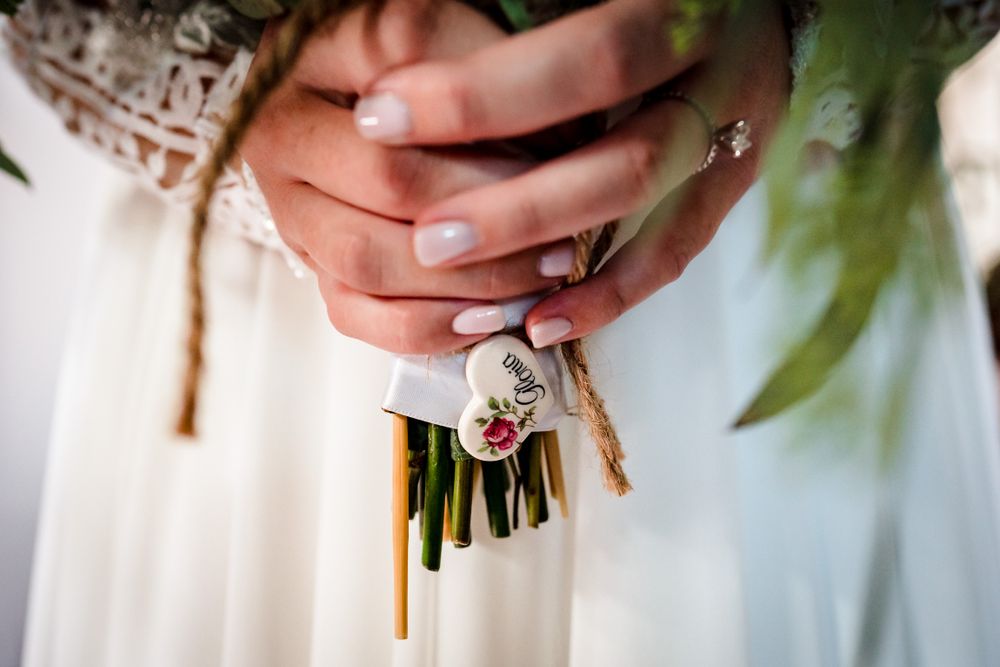 Wedding bouquet held by hands wearing elegant rings and neutral nail polish.