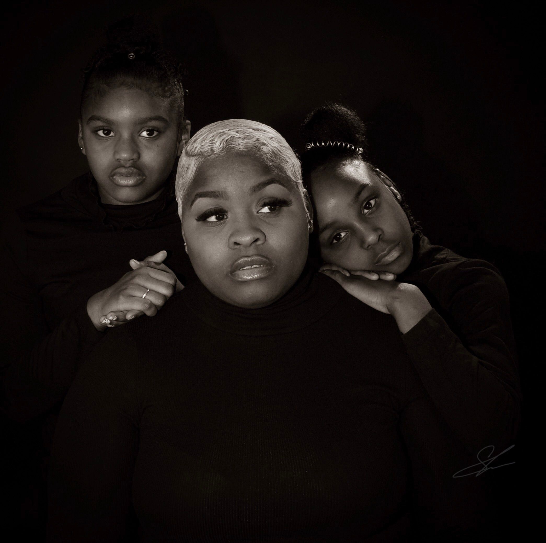 Artistic black and white portrait of three people in dark clothing.