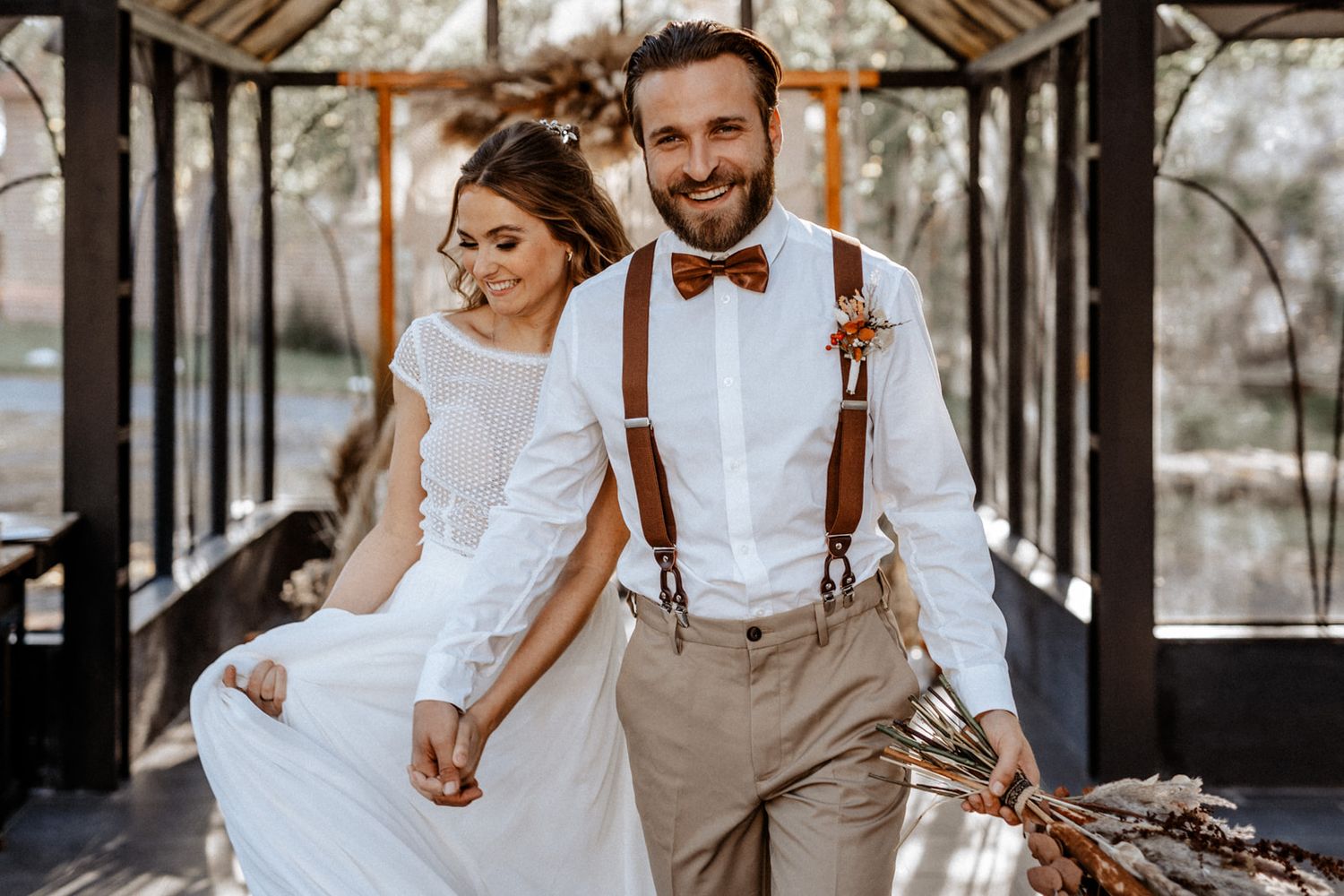 Rustic wedding photo showcasing a couple in bohemian style attire with suspenders and bow tie.