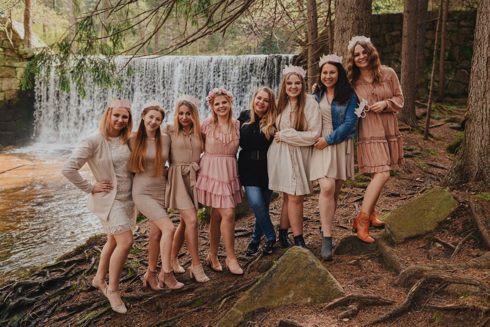 Group photo of friends in floral dresses gathered near a waterfall in a forest setting.