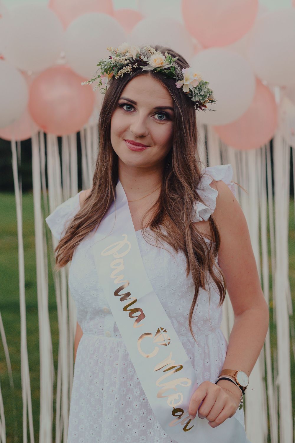 A white lace dress and floral crown against a backdrop of pink balloons and white streamers.