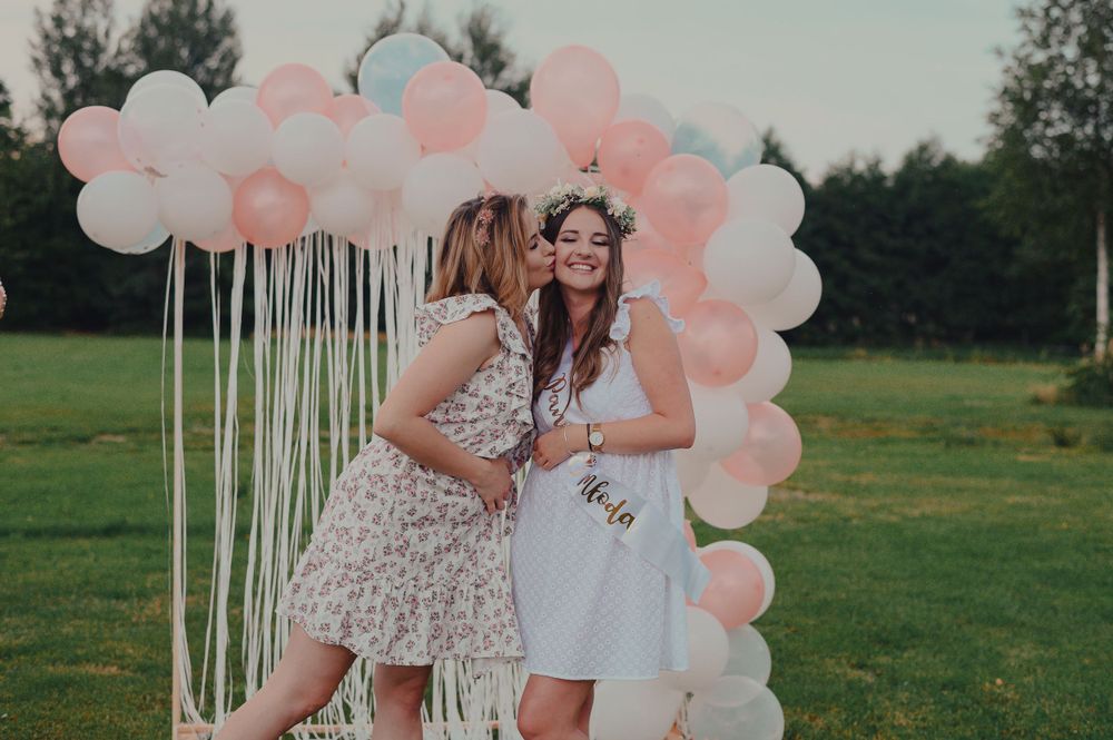 Outdoor celebration with pink balloon arch and white streamers in a field setting.