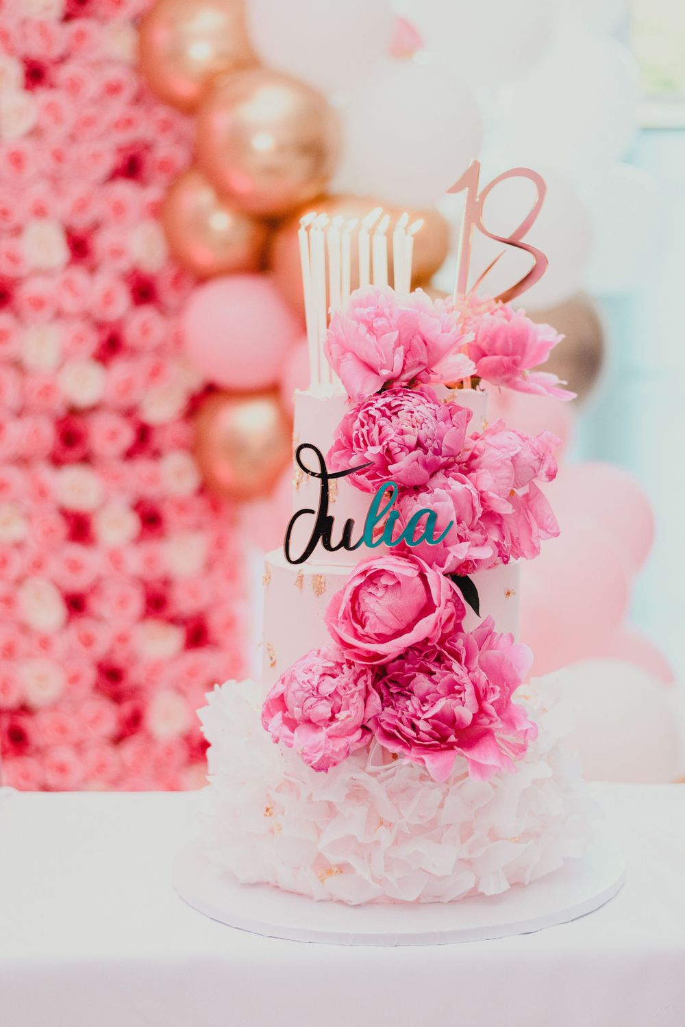 Pink and white cake decorated with fresh flowers against a floral backdrop.