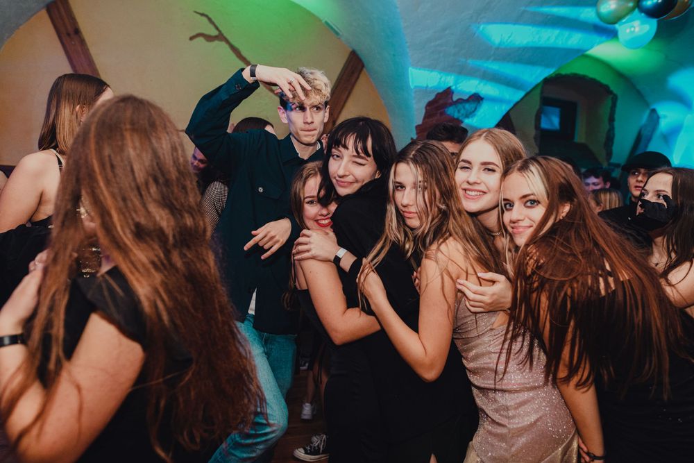 Crowded dance floor with party-goers dancing under vibrant blue and green lighting.