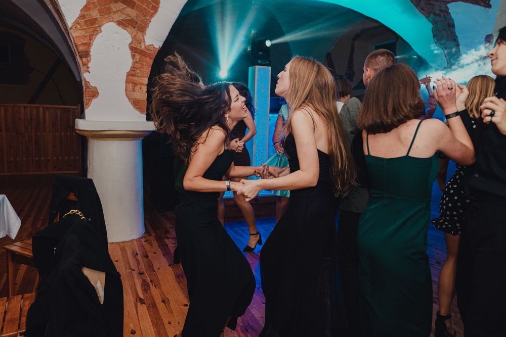 People dancing under turquoise lighting at an indoor party venue with exposed brick walls.