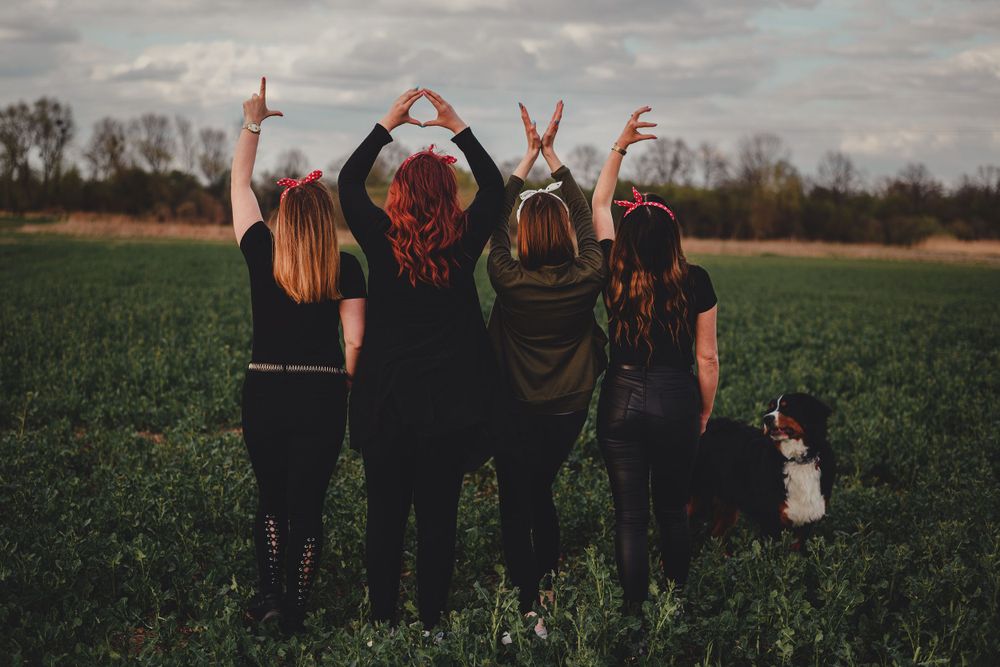Friends forming the word LOVE with their hands against a cloudy sky in a field.
