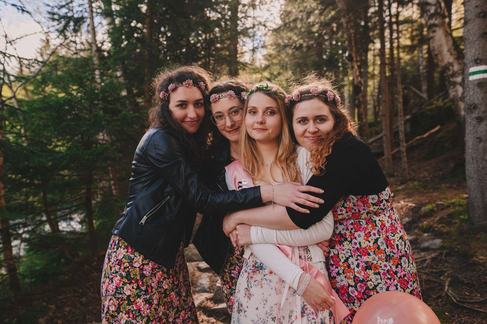 Women in floral print dresses posing together for outdoor photo shoot in wooded setting.