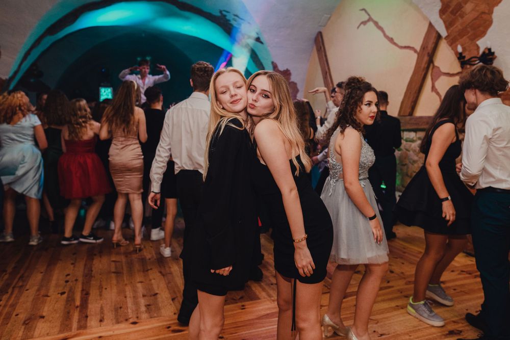 Party guests dancing on wooden floor under colorful mood lighting.