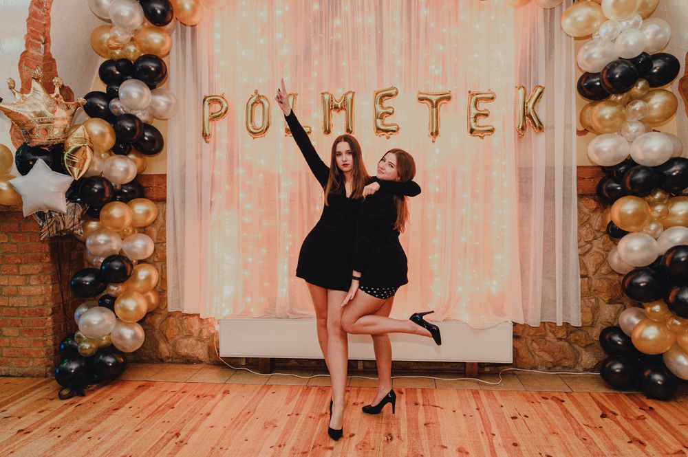 Party venue decorated with black, white and gold balloon arch arrangements and festive lighting for celebration.