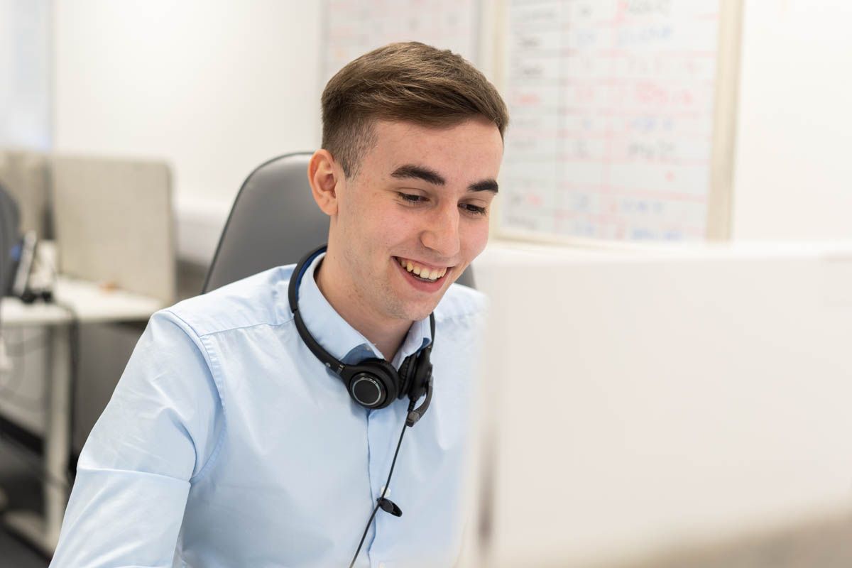 Young professional with headphones smiling while working at computer desk.