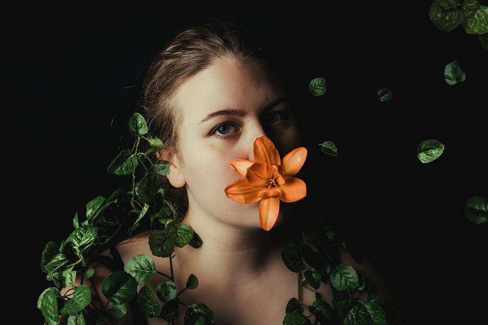 Dark portrait with orange lily and green ivy creating nature-inspired composition.