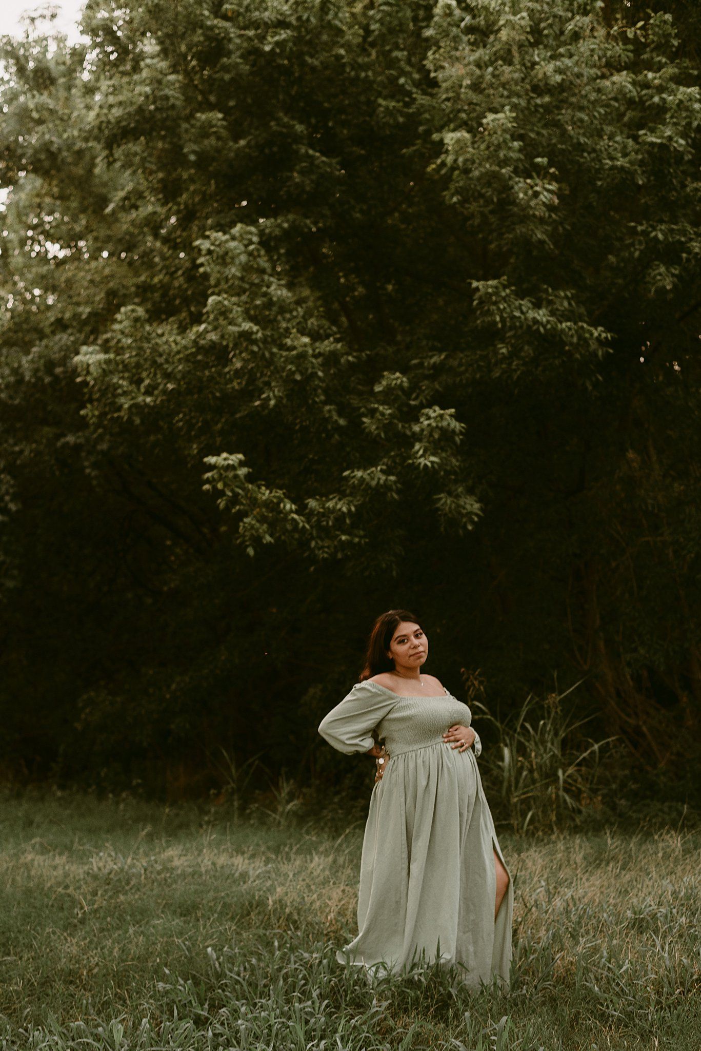 Ethereal maternity portrait with dramatic forest canopy background.