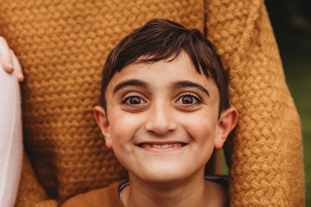Close-up portrait of child wearing orange sweater with bright smile.