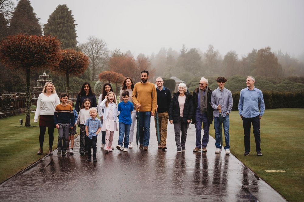 A family group stands together on a rainy day in a park with autumn trees in the background.