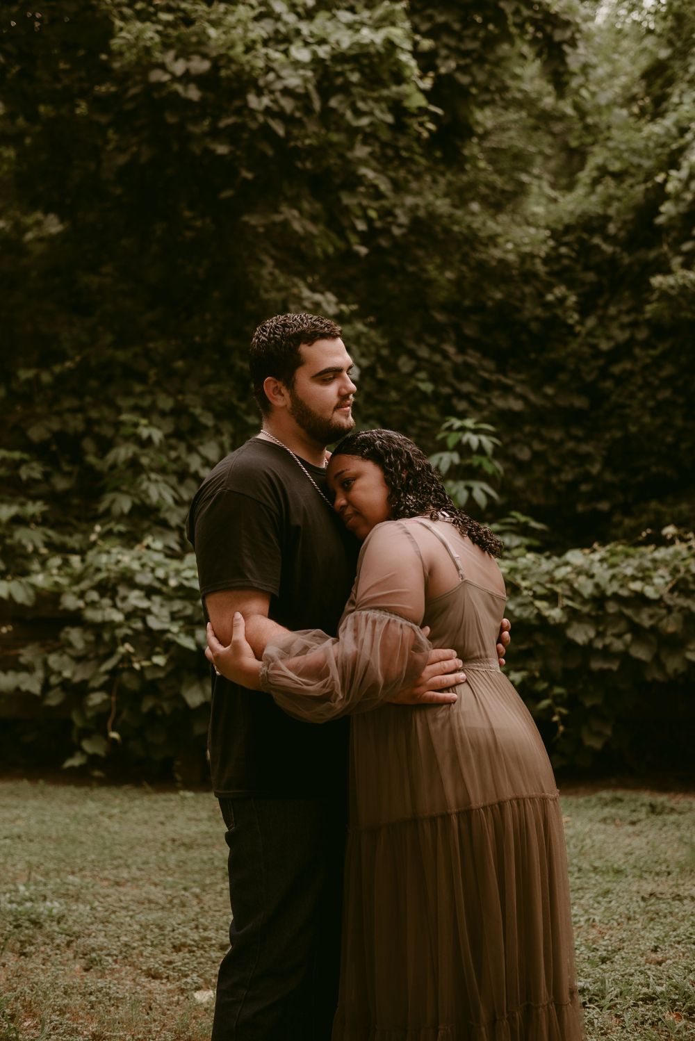 A tender moment between a couple embracing against a backdrop of green foliage.