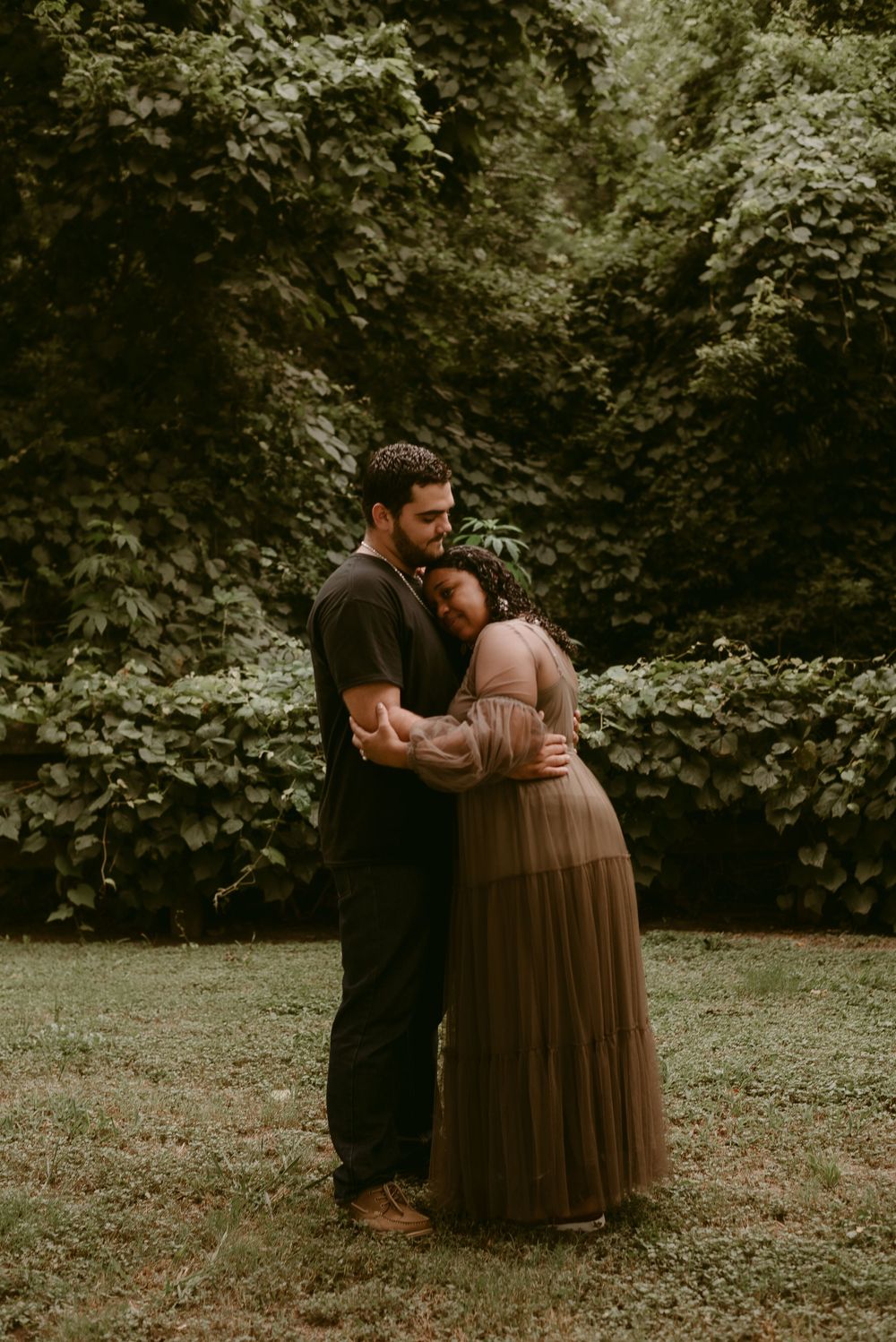A romantic couple embrace in a dreamy outdoor setting with lush greenery.