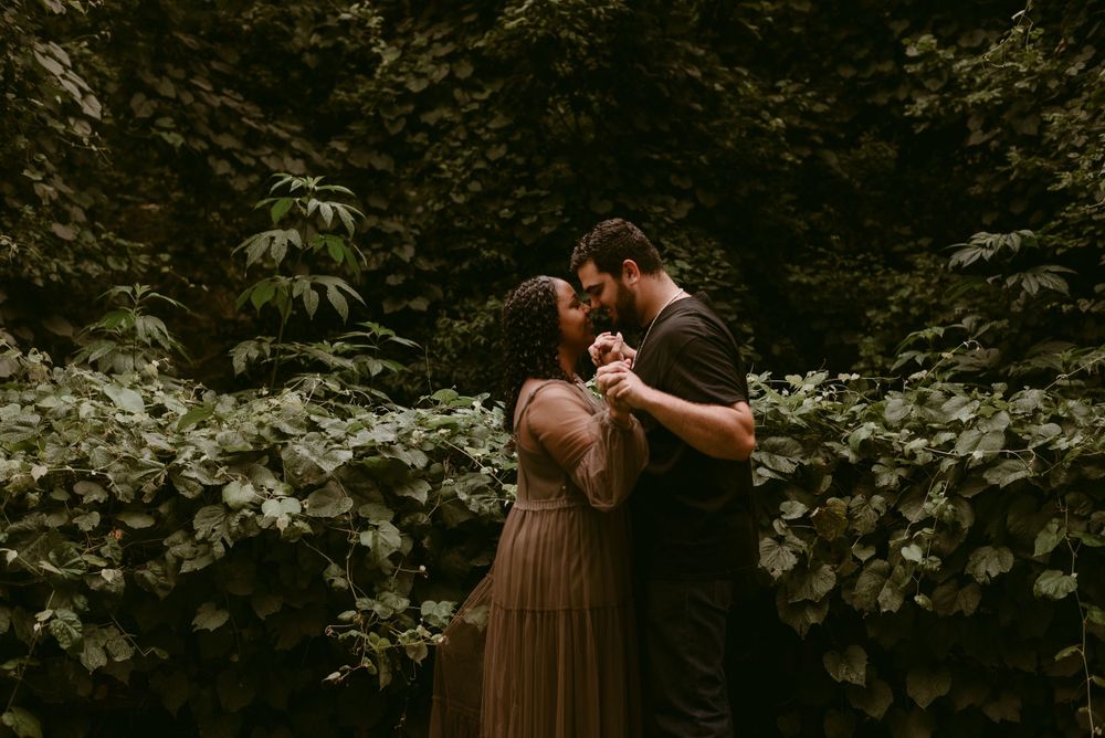 A romantic couple shares an intimate moment in a lush green garden setting with moody lighting.