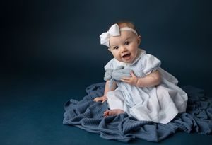 Studio portrait with white dress against deep blue backdrop and fabric styling.