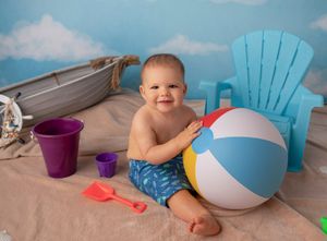 Beach themed photo setup with toy boat, blue chair and beach ball props.