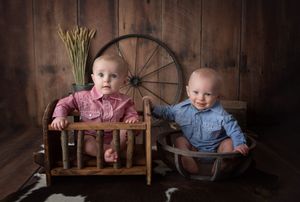 Two babies in rustic outfits posed with vintage wooden furniture and wagon wheel decor.