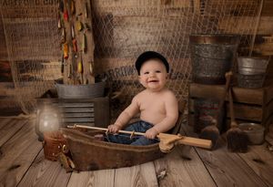 Baby sitting in vintage wooden boat prop with rustic decor and fishing equipment.
