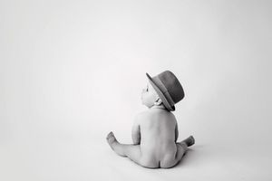Artistic black and white portrait of a baby wearing a fedora hat sitting on white background.
