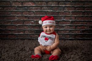 Baby in festive outfit sitting against brick wall background.