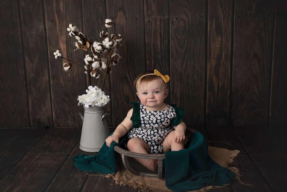 Baby in leopard print outfit sits with cotton stems and teal fabric during studio portrait.