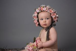 Baby wearing floral crown poses against grey backdrop during professional photo session.