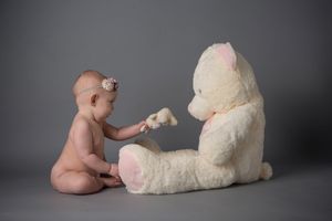 Baby interacts with large cream teddy bear during studio portrait session.
