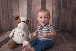 Baby in striped shirt sits next to personalized plush dog during portrait session.