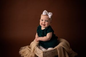 Baby wearing green dress and bow sits on wooden crate with gold tulle fabric.