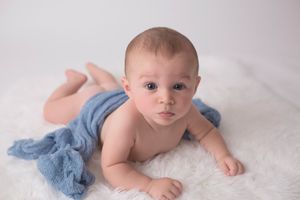 Baby lying on white blanket with light blue fabric draping.