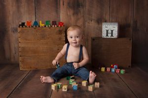 Baby in denim playing with wooden alphabet blocks on rustic wooden floor.
