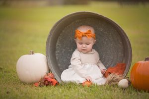Baby in white dress sitting in galvanized tub with pumpkins and fall decor.